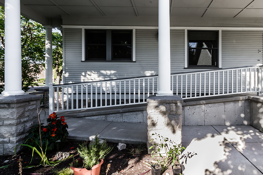 A concrete switchback ramp provides a shallow, accessible pathway past a garden to a front entrance several feet above ground level.